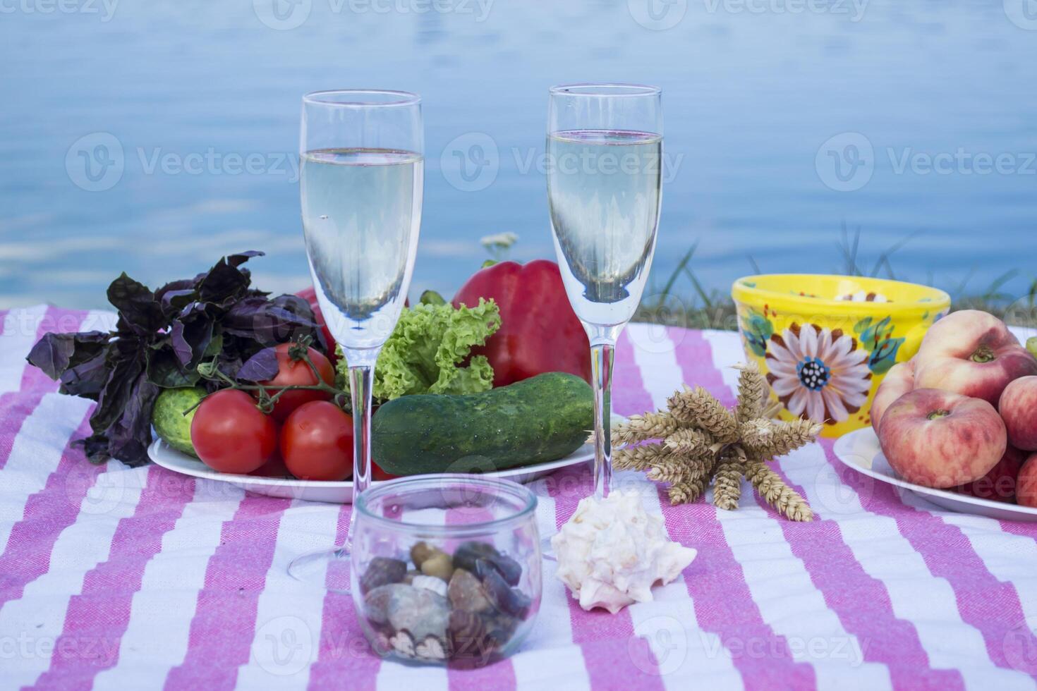 Beautiful picnic with fruits, vegetables and glasses of wine near lake. photo