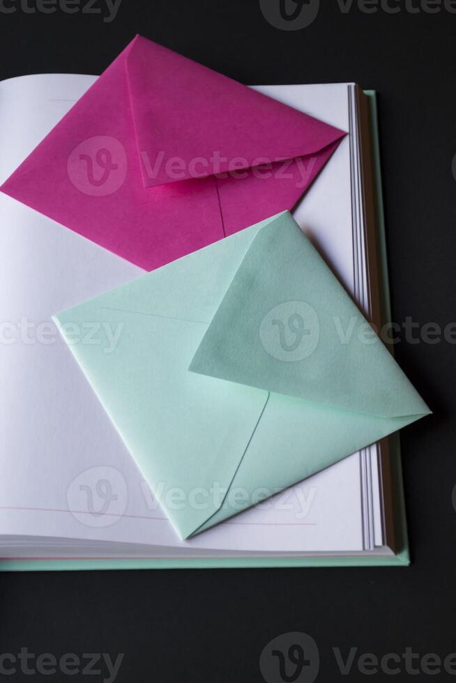 The turquoise and pink colors envelopes on the opened notepad, close up. photo