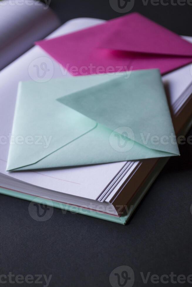 The turquoise and pink colors envelopes on the opened notepad, close up. photo