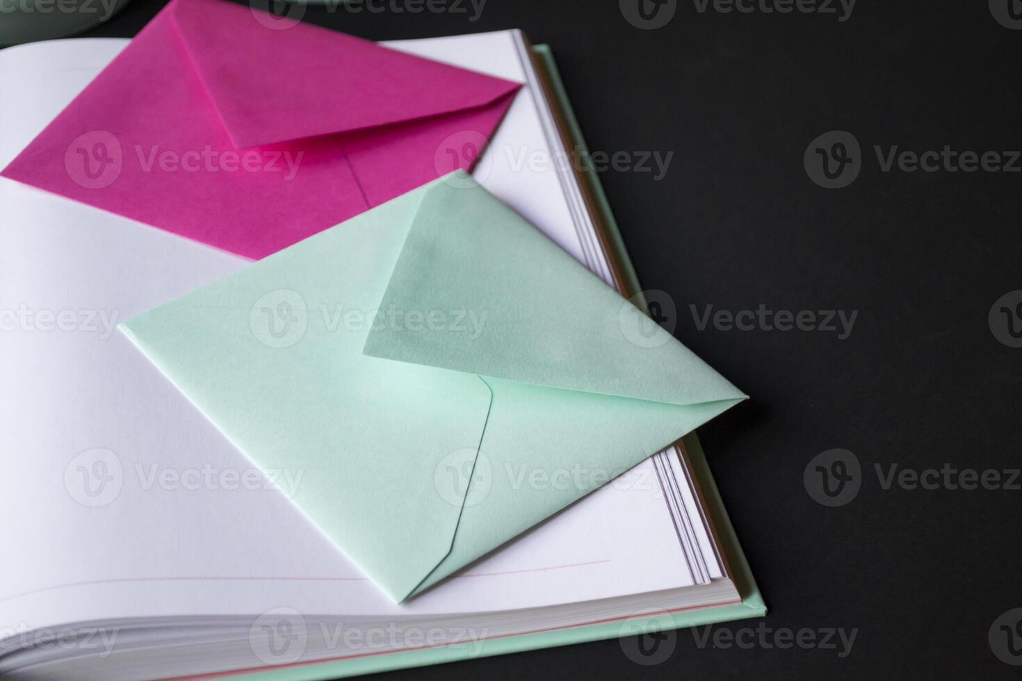 The turquoise and pink colors envelopes on the opened notepad, close up. photo