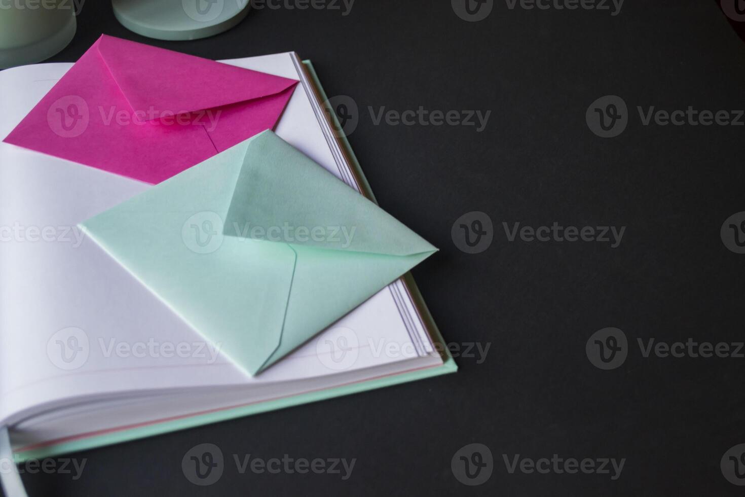 The turquoise and pink colors envelopes on the opened notepad, close up. photo