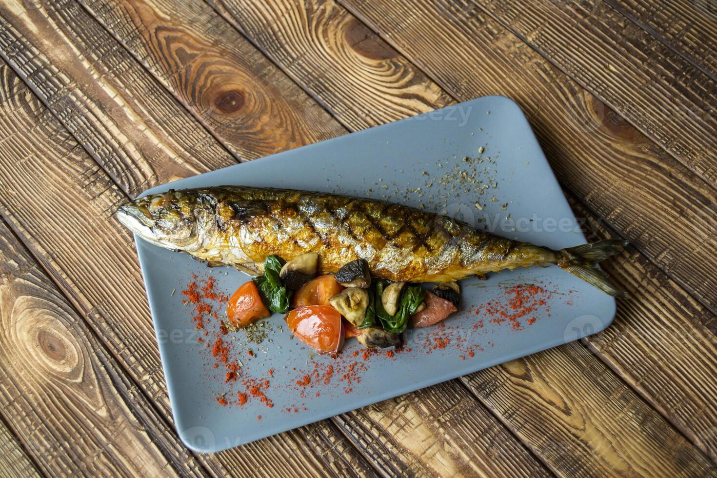 Grilled fish with vegetables in a plate on a wooden table. photo