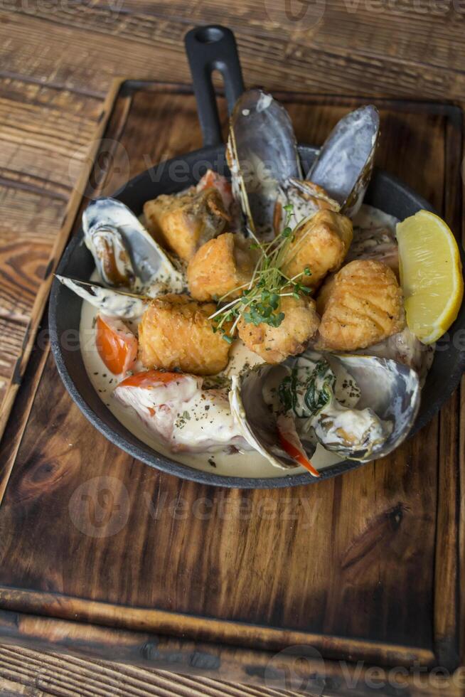 Fried fish with mussels, sauce and lemon on a wooden table. photo