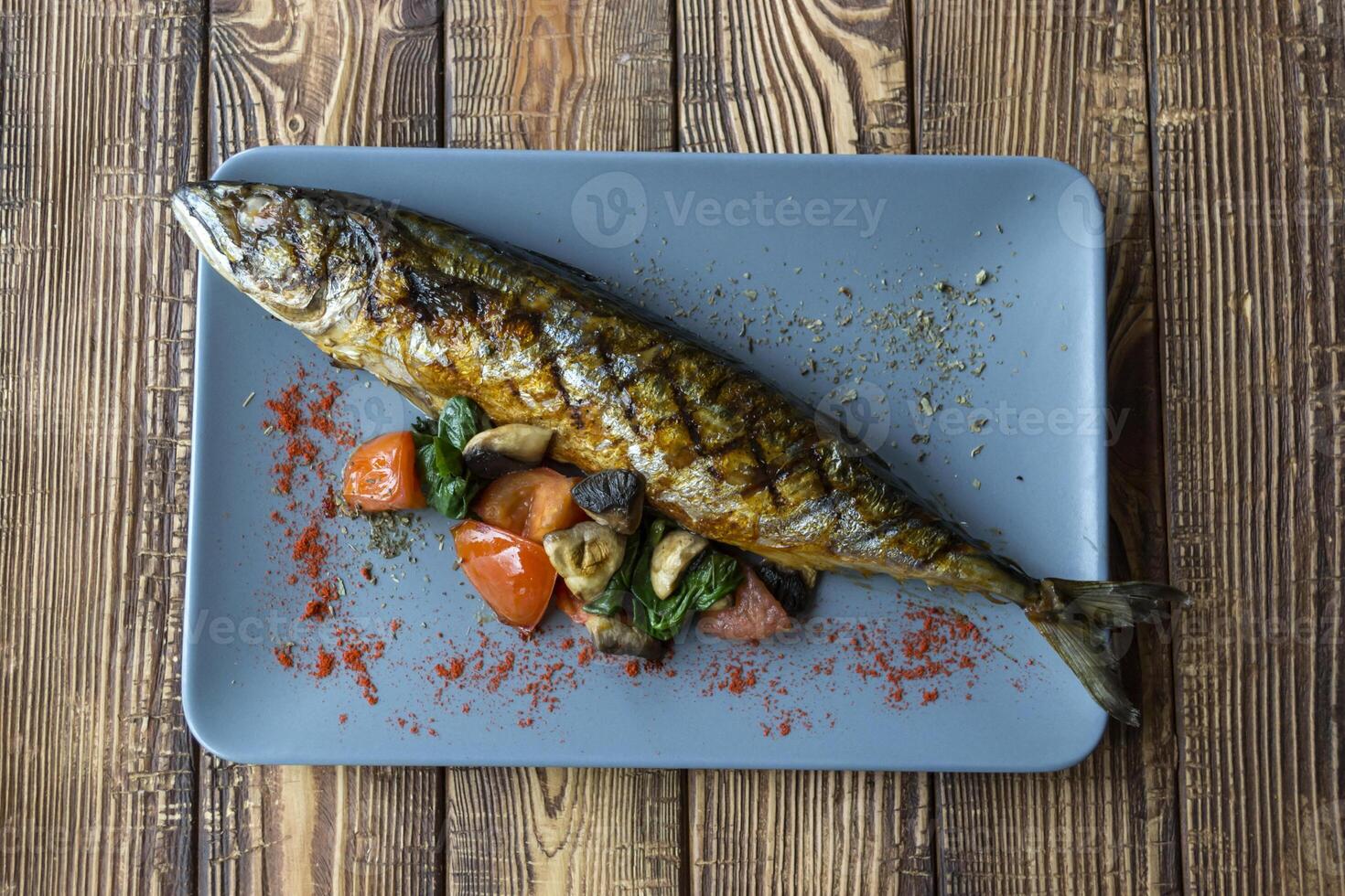 Grilled fish with vegetables in a plate on a wooden table. photo