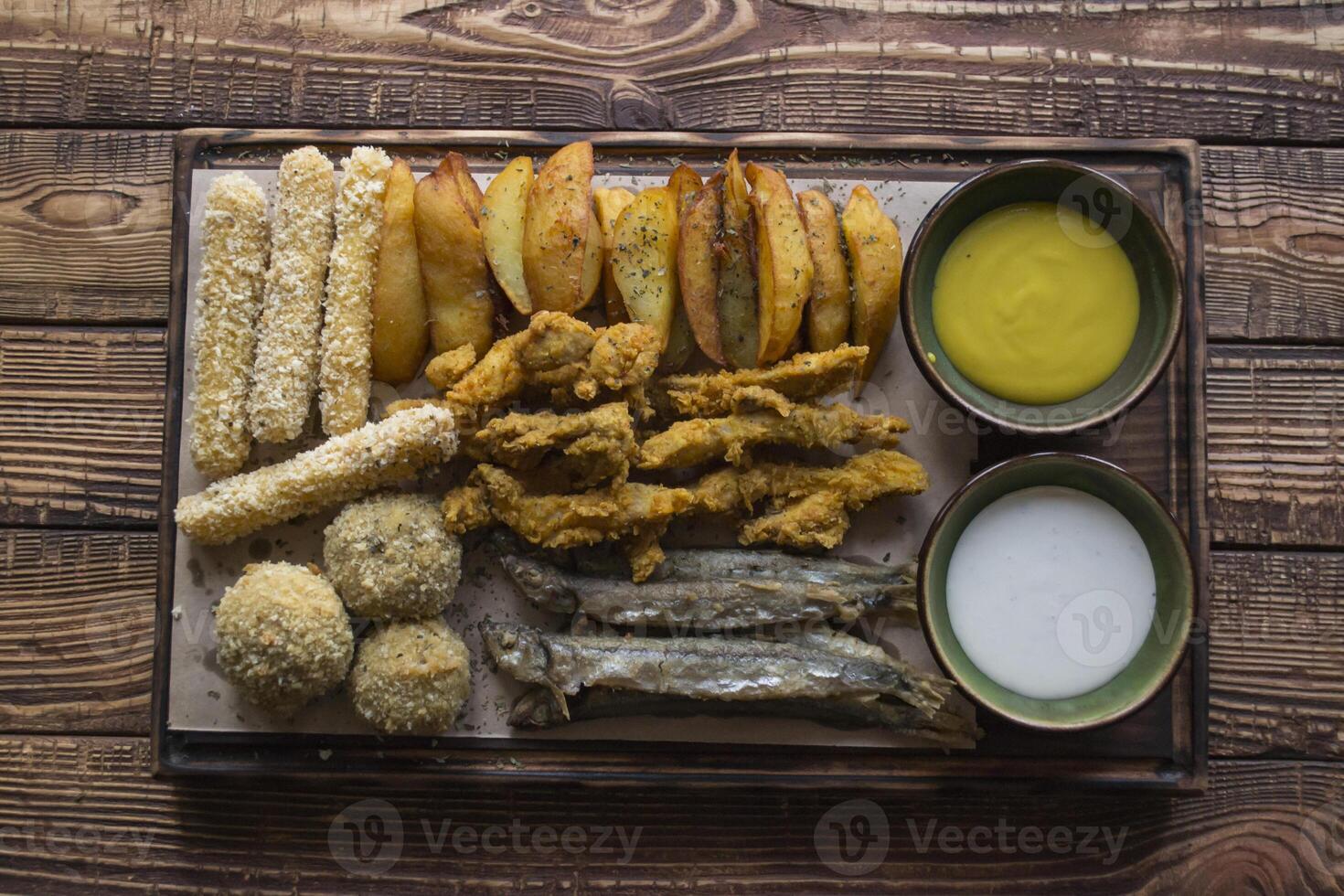 Fried potatoes with fish, cheese sticks and sauces. photo
