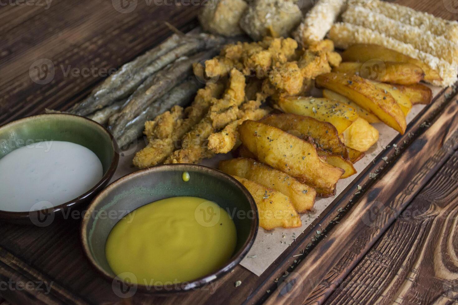 Fried potatoes with fish, cheese sticks and sauces. photo