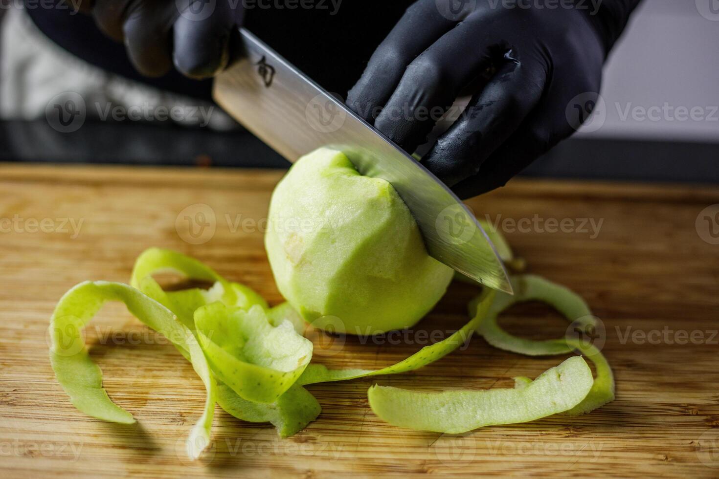 Person with black gloves peeling and cutting an apple with japanese knife photo