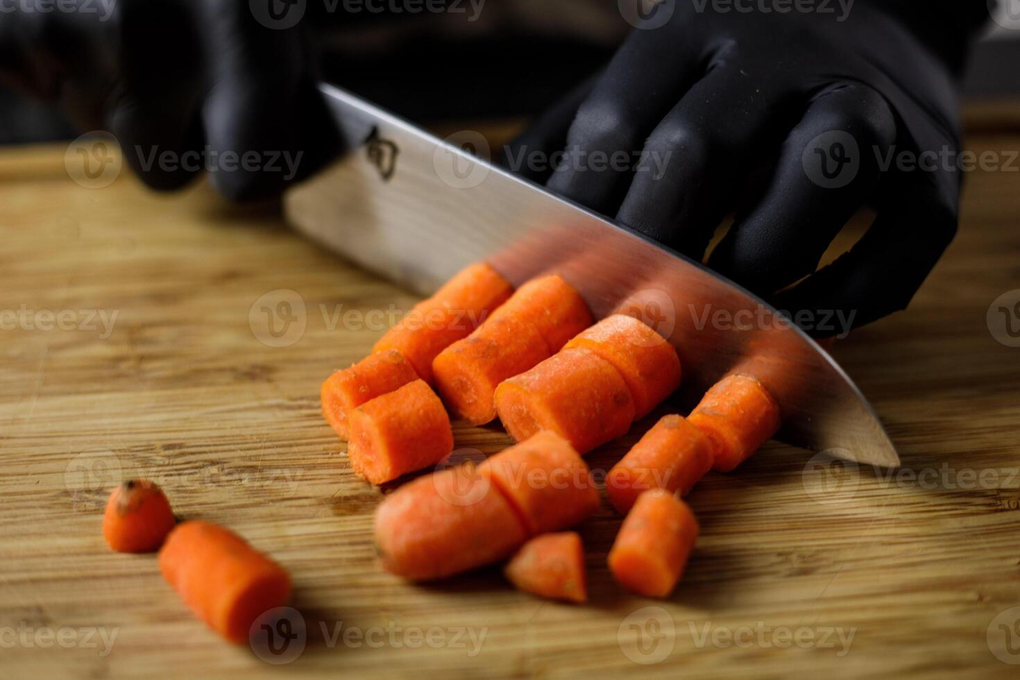 Person with black gloves cuts carrots in pieces on wooden cutting board photo