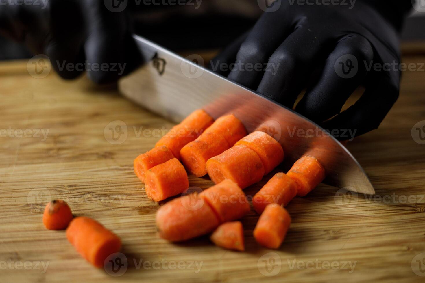 persona con negro guantes cortes zanahorias en piezas en de madera corte tablero foto