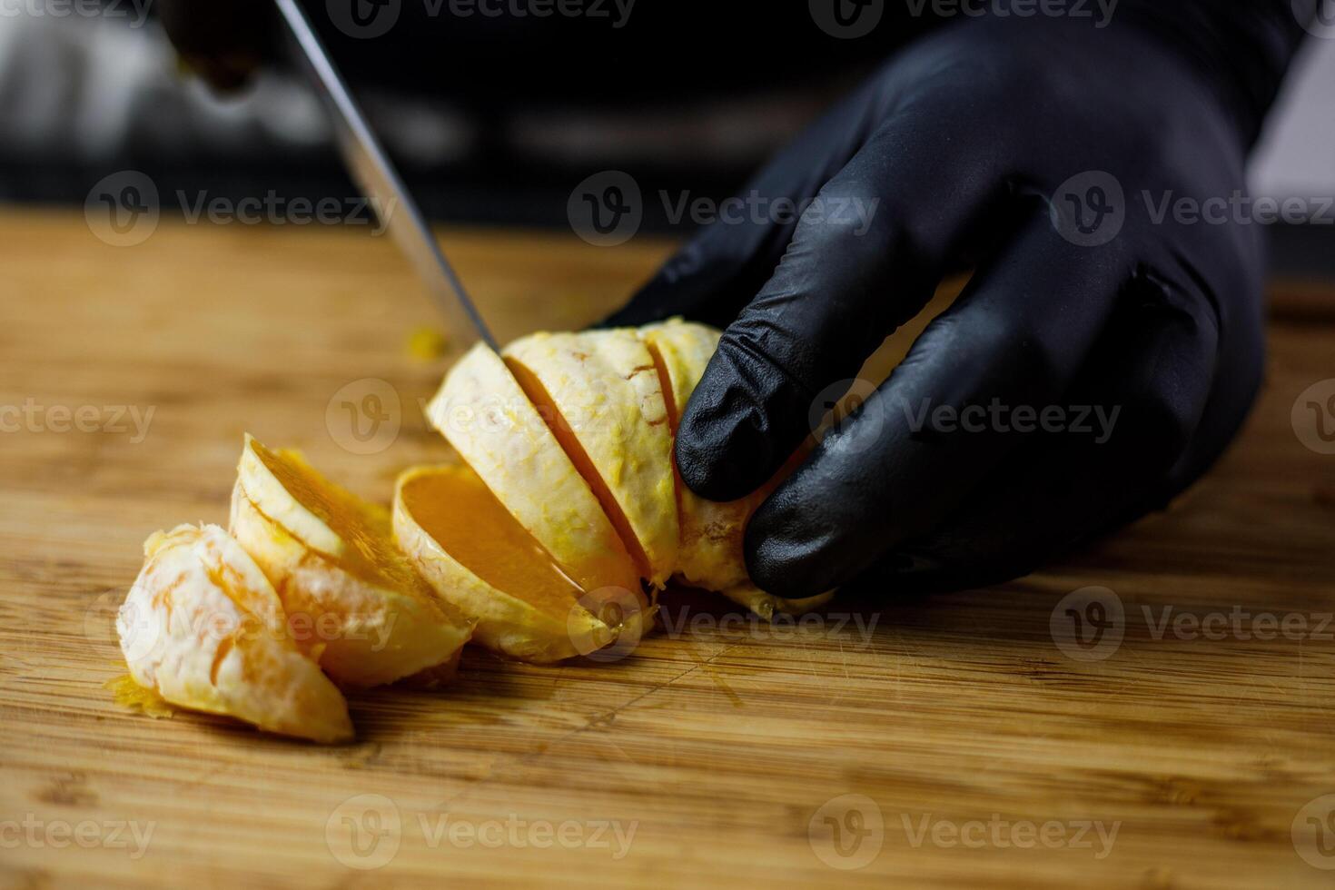 Person with black gloves cuts peeled orange on wooden cutting board into pieces photo
