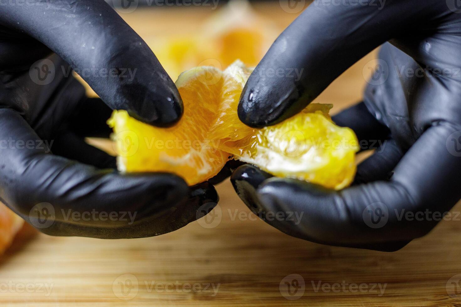 Person with black gloves splitting peeled orange in half wooden cutting board photo