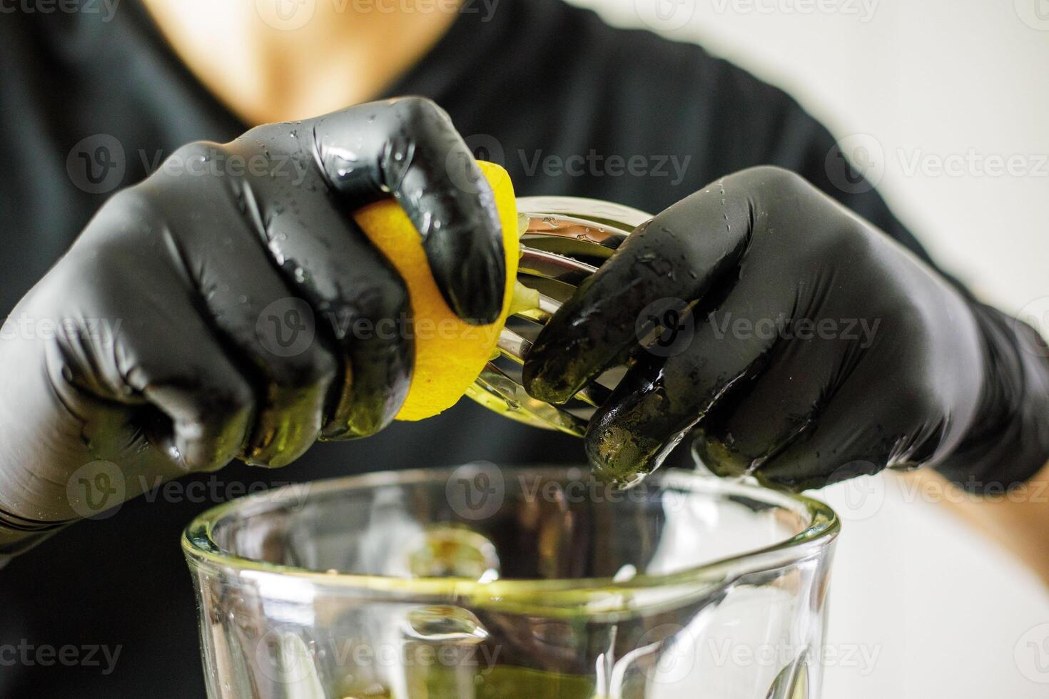 Person with black gloves squeezing lemon into blender for smoothie preparation photo