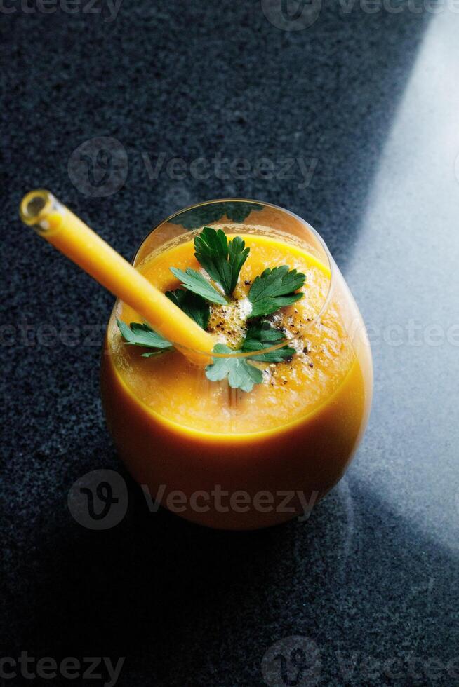 Mango Carrot Apple Smoothie in a glass on dark background with glass straw photo