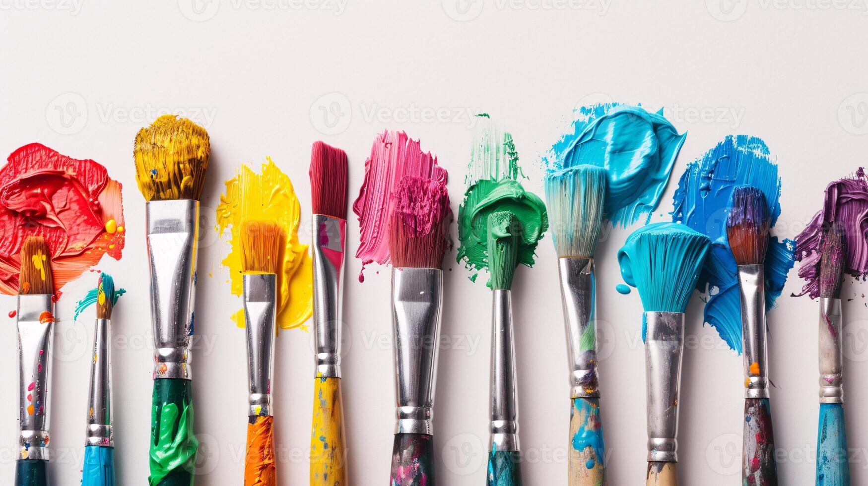 An arrangement of colorful paintbrushes dipped in various hues of paint on a pristine white surface photo