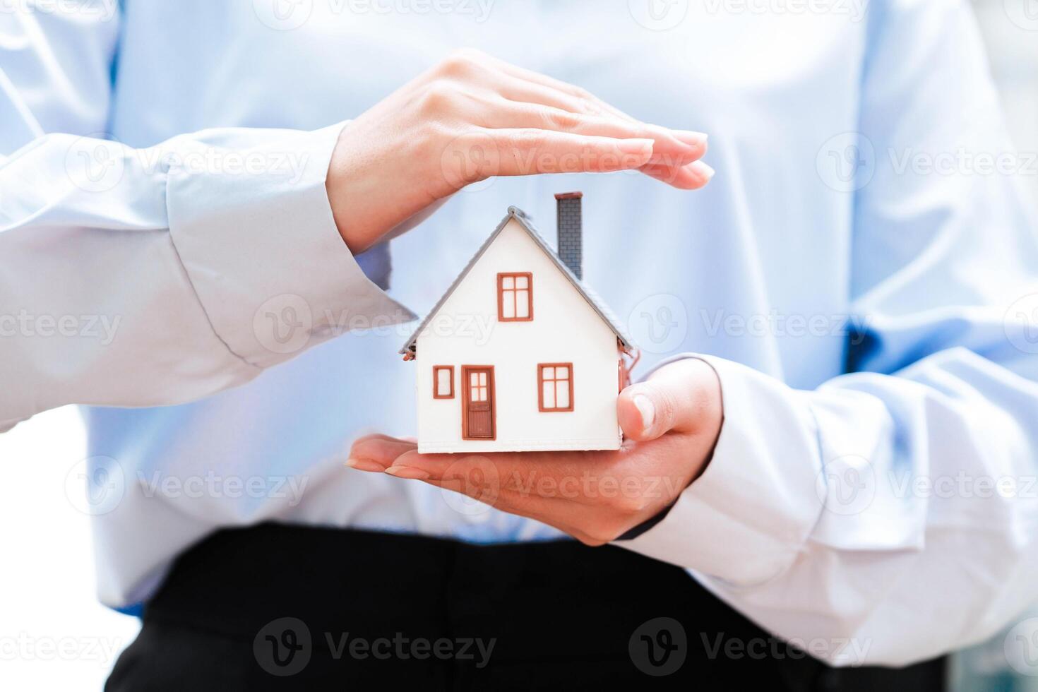 Hands holding a small house model, depicting safety and security in homeownership. photo