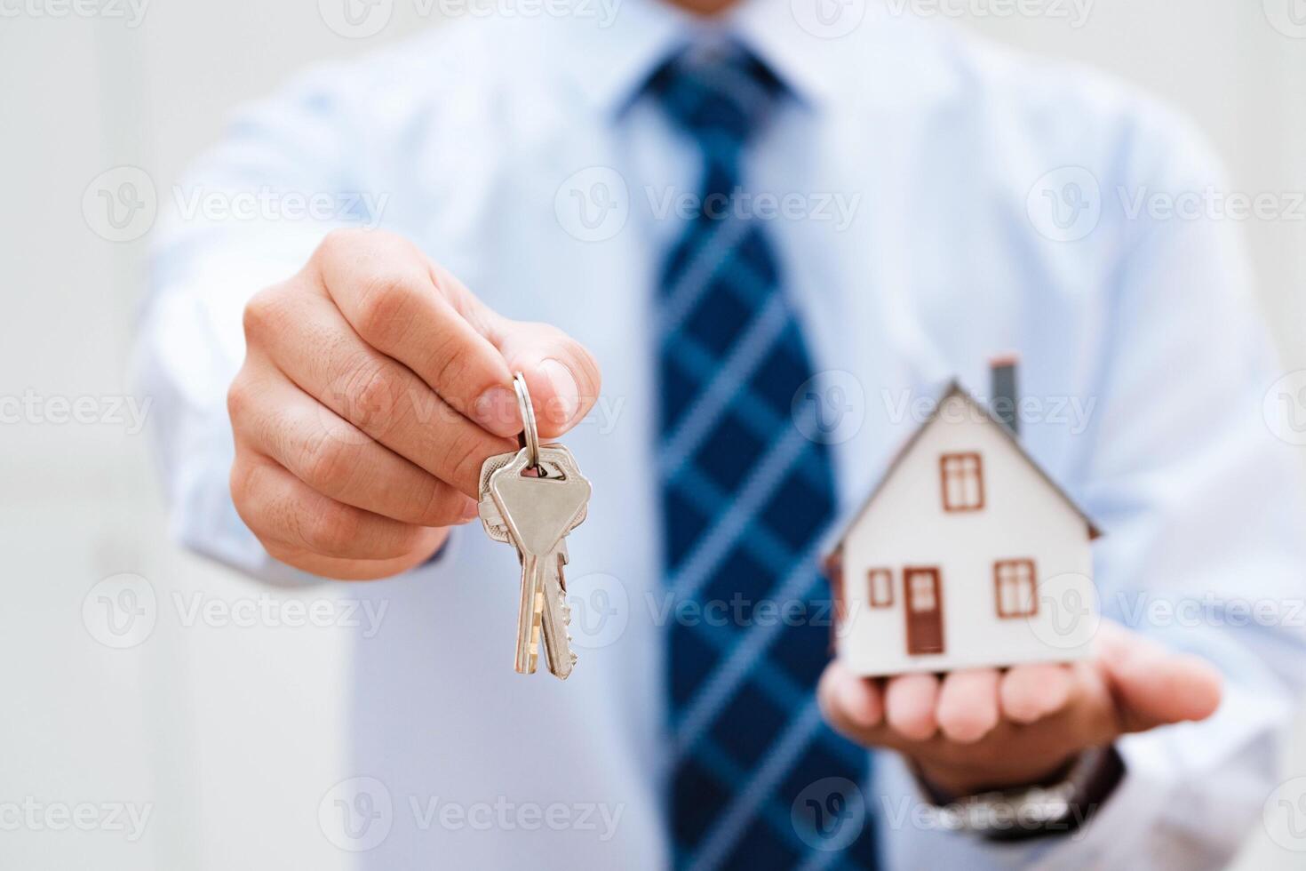 Estate agent offers house keys and model home, illustrating successful ownership. photo
