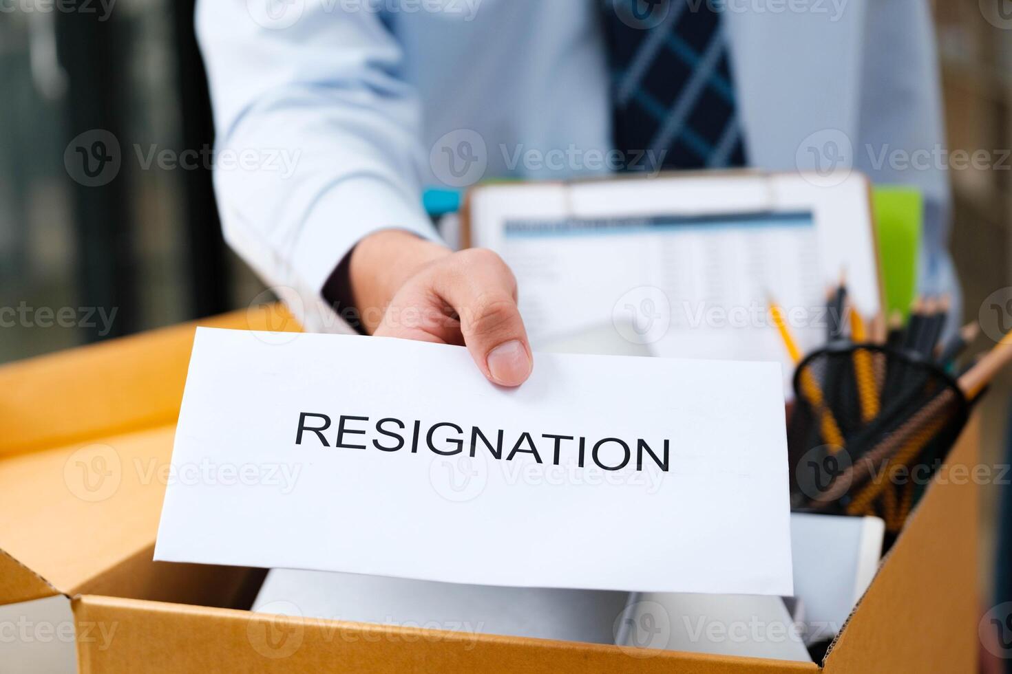 Man's hand presenting a resignation letter, office box with belongings in the back. photo