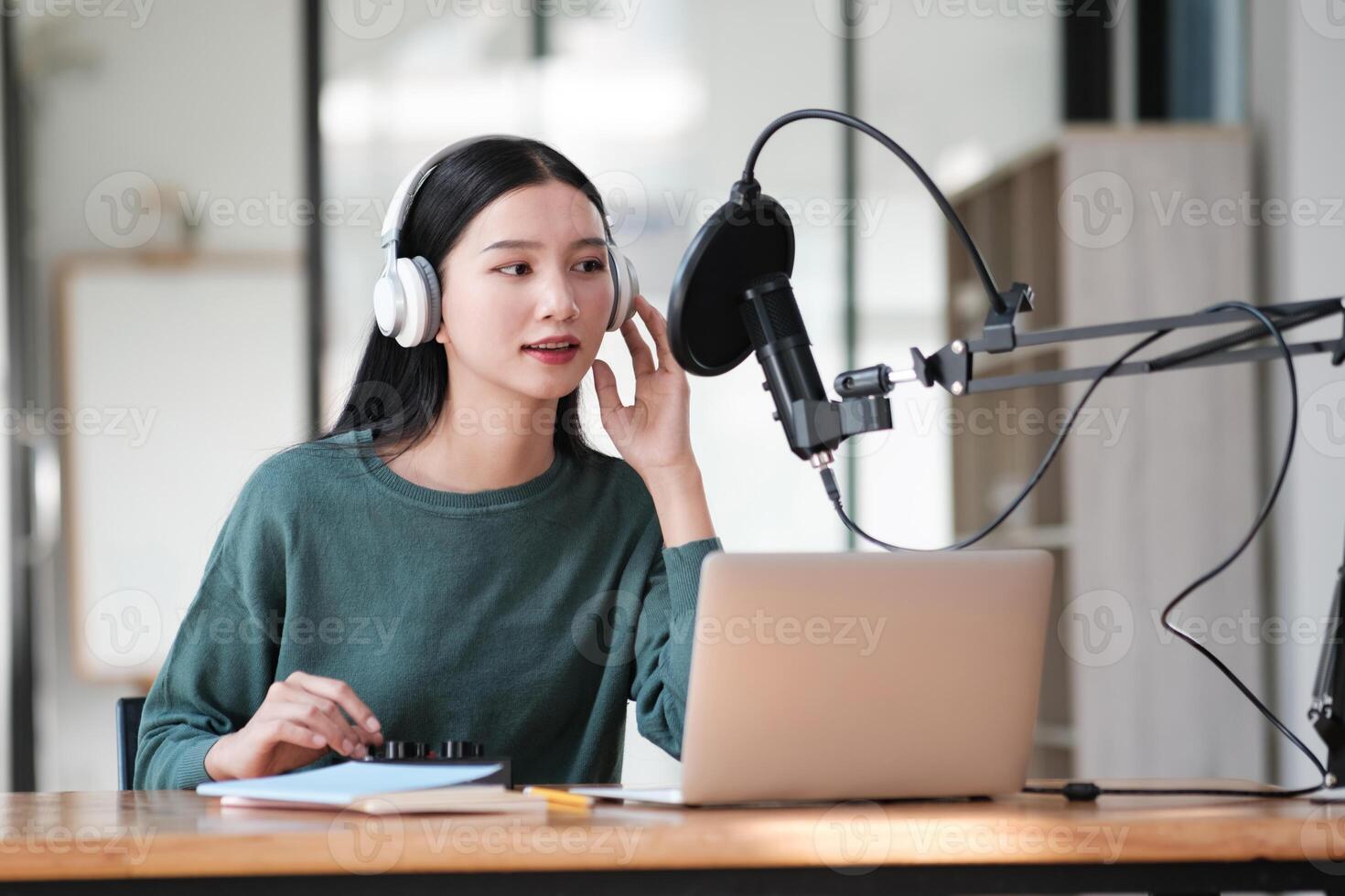 A woman wearing headphones is sitting at a desk with a laptop and a microphone photo