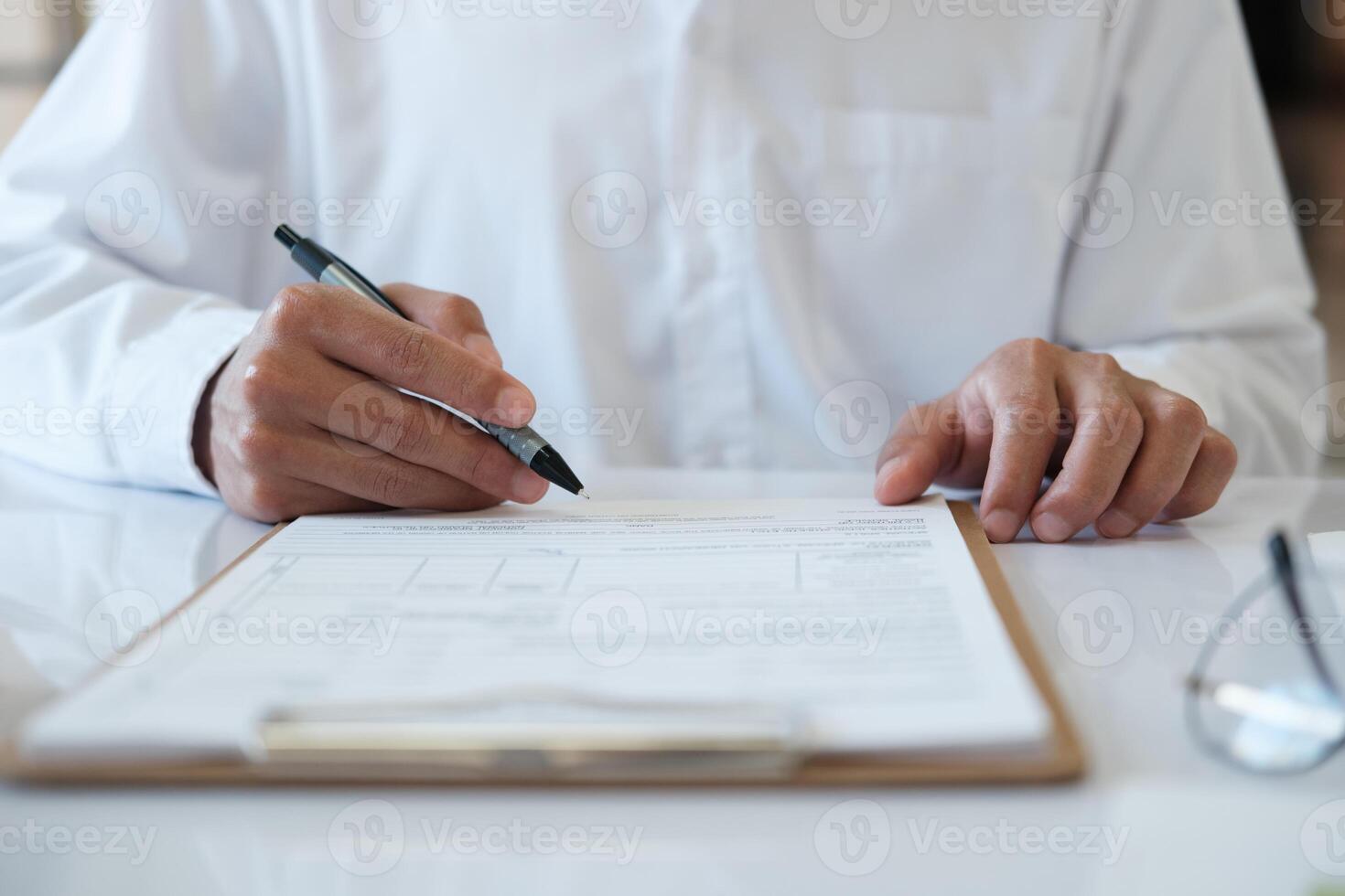 A man is writing on a piece of paper with a pen photo