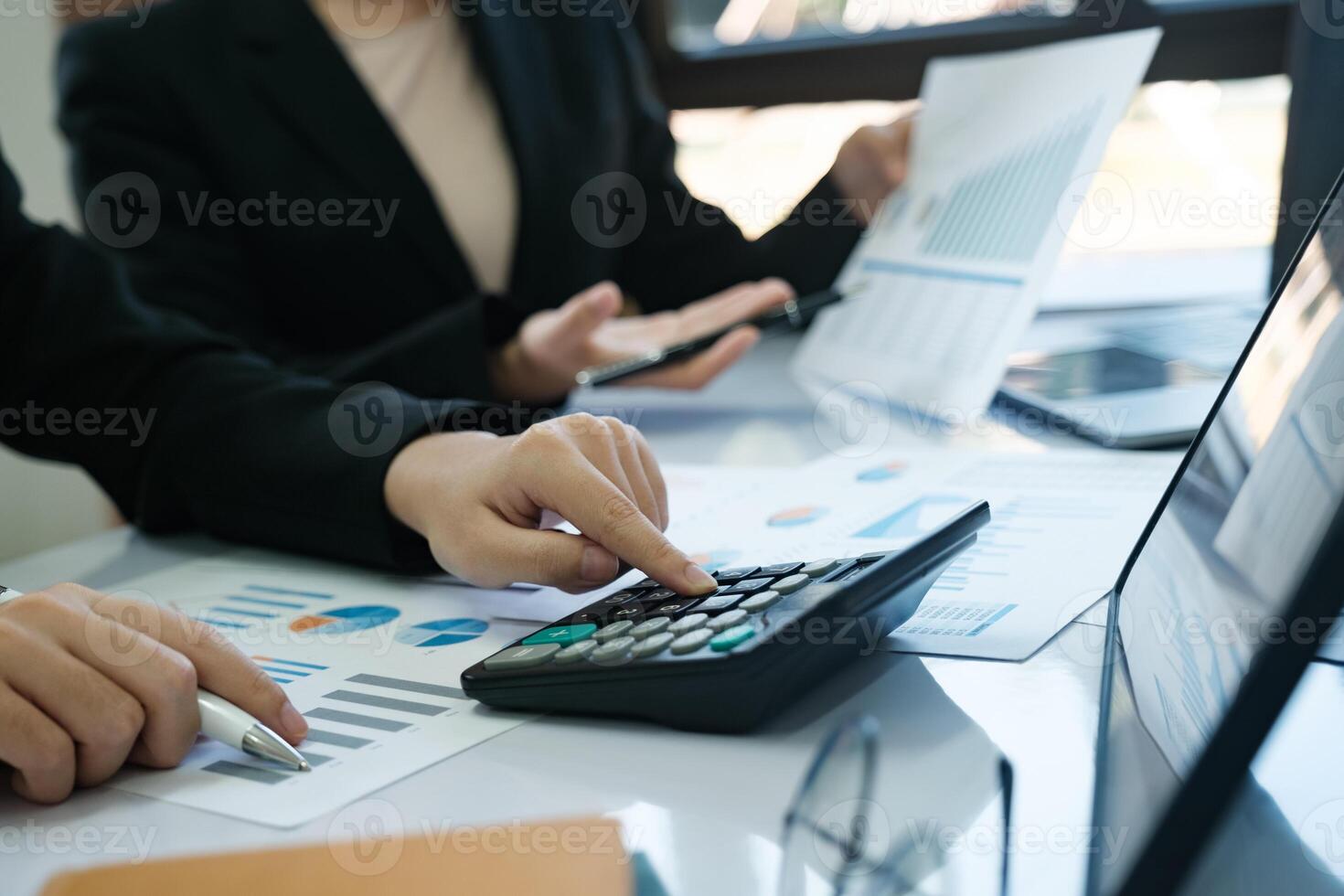 Two women are working on a spreadsheet, one of them pointing at a calculator photo