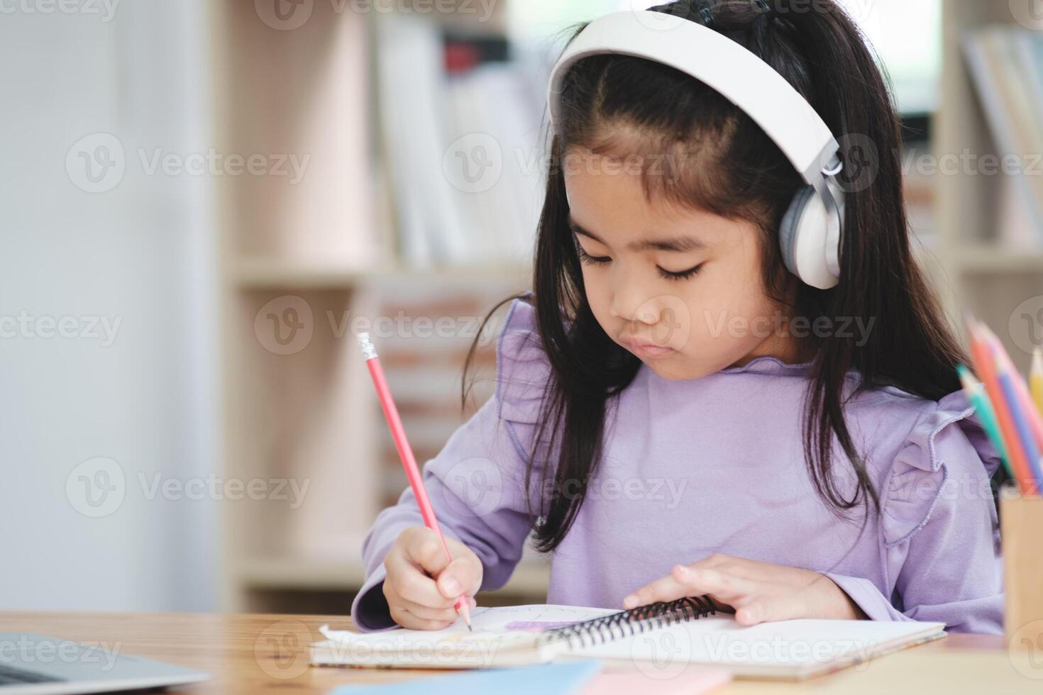 A young girl is sitting at a desk with a pencil and a notebook photo