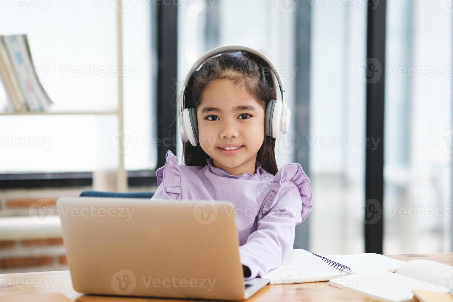 A young girl is sitting at a desk with a laptop and a notebook photo