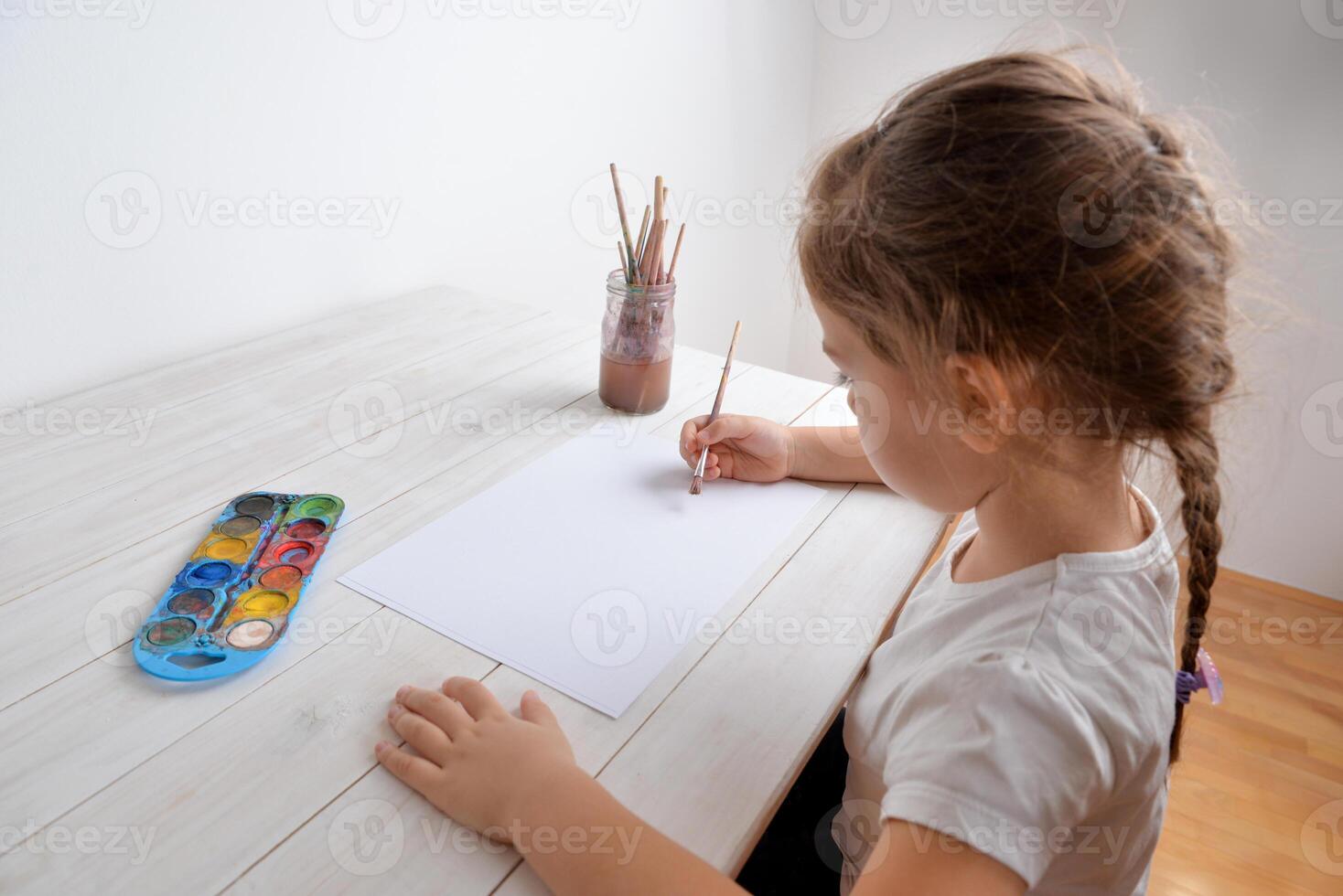 Little girl paints with water colors on white paper. Concept of creativity, art, childhood, imagination, and artistic expression photo