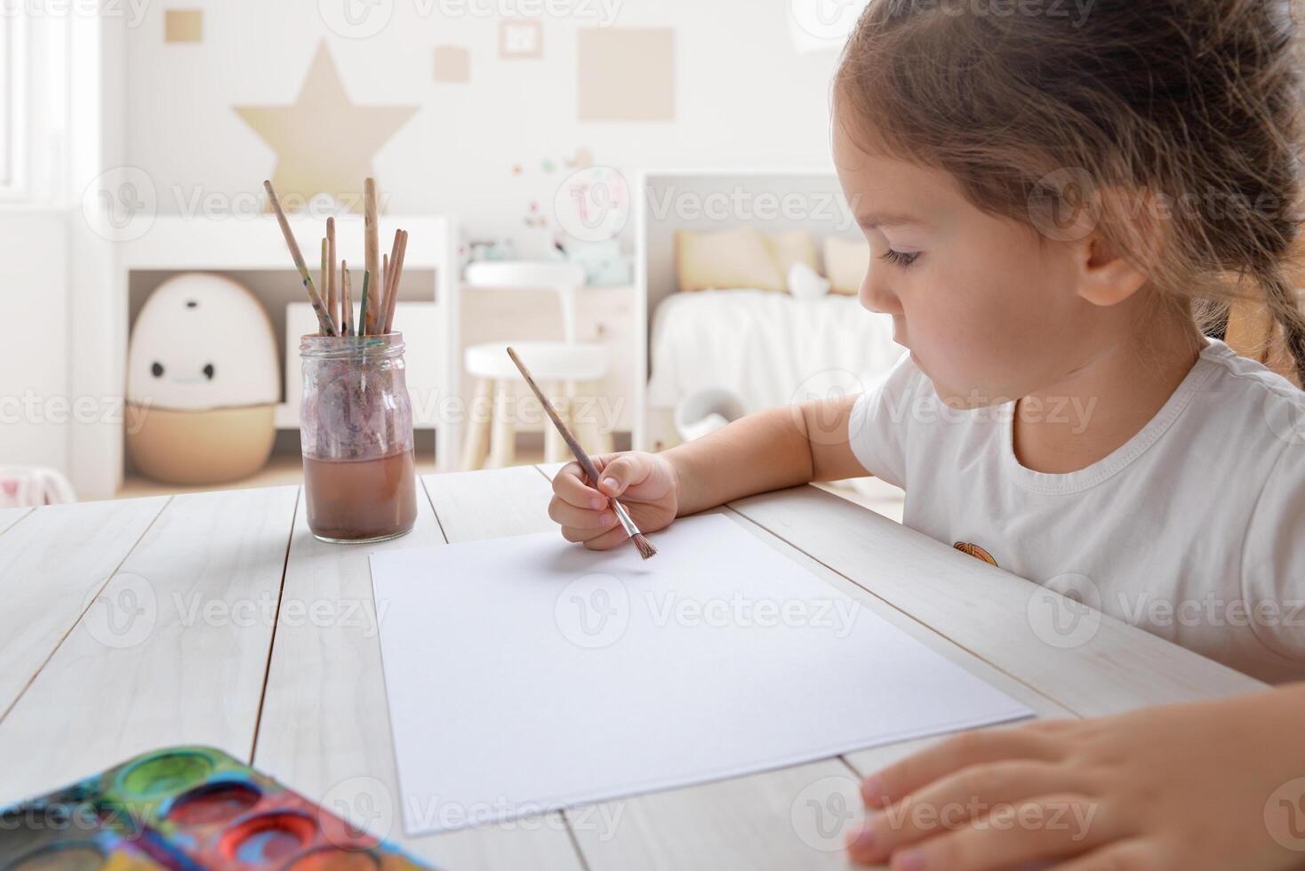 Young girl painting with watercolors on white paper in her room. Ideal for children's creativity or artistic concepts photo