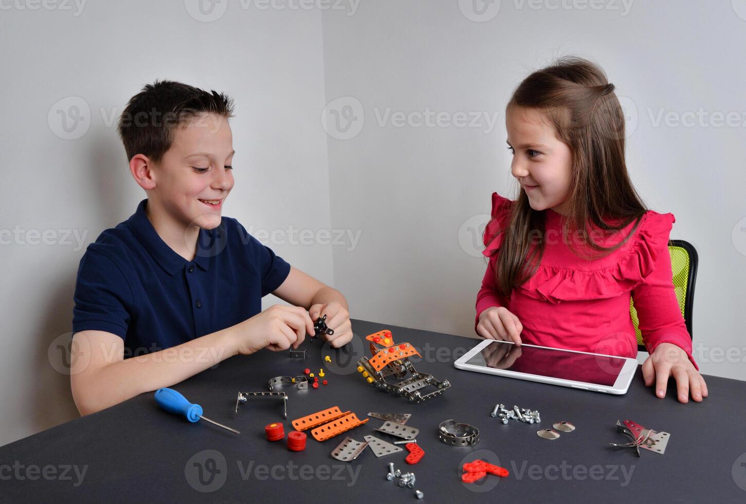 Girl and boy build robot with tools, programming with tablet. Concept of education, creativity, and technology exploration for children photo