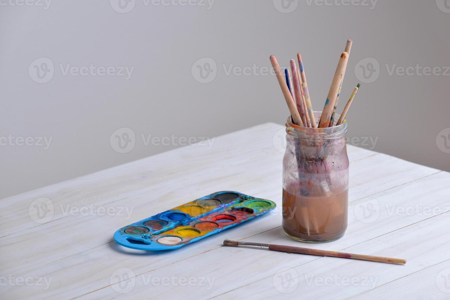 Jar with paintbrushes on work table with watercolors. Copy space aside. Ideal for art supplies, creativity, or painting concepts photo