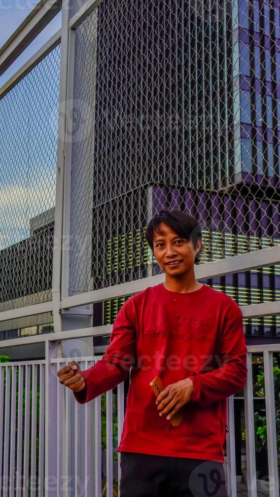 Javanese man in red is looking at his cellphone with a happy expression. photo