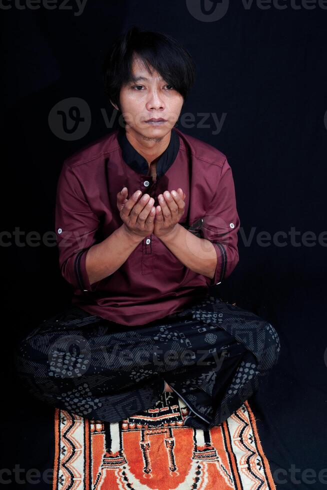 front view of a man praying on a prayer mat with a black background. photo