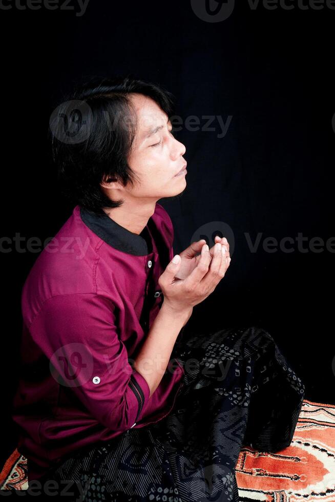 side view of a man praying on a prayer mat on a black background. photo