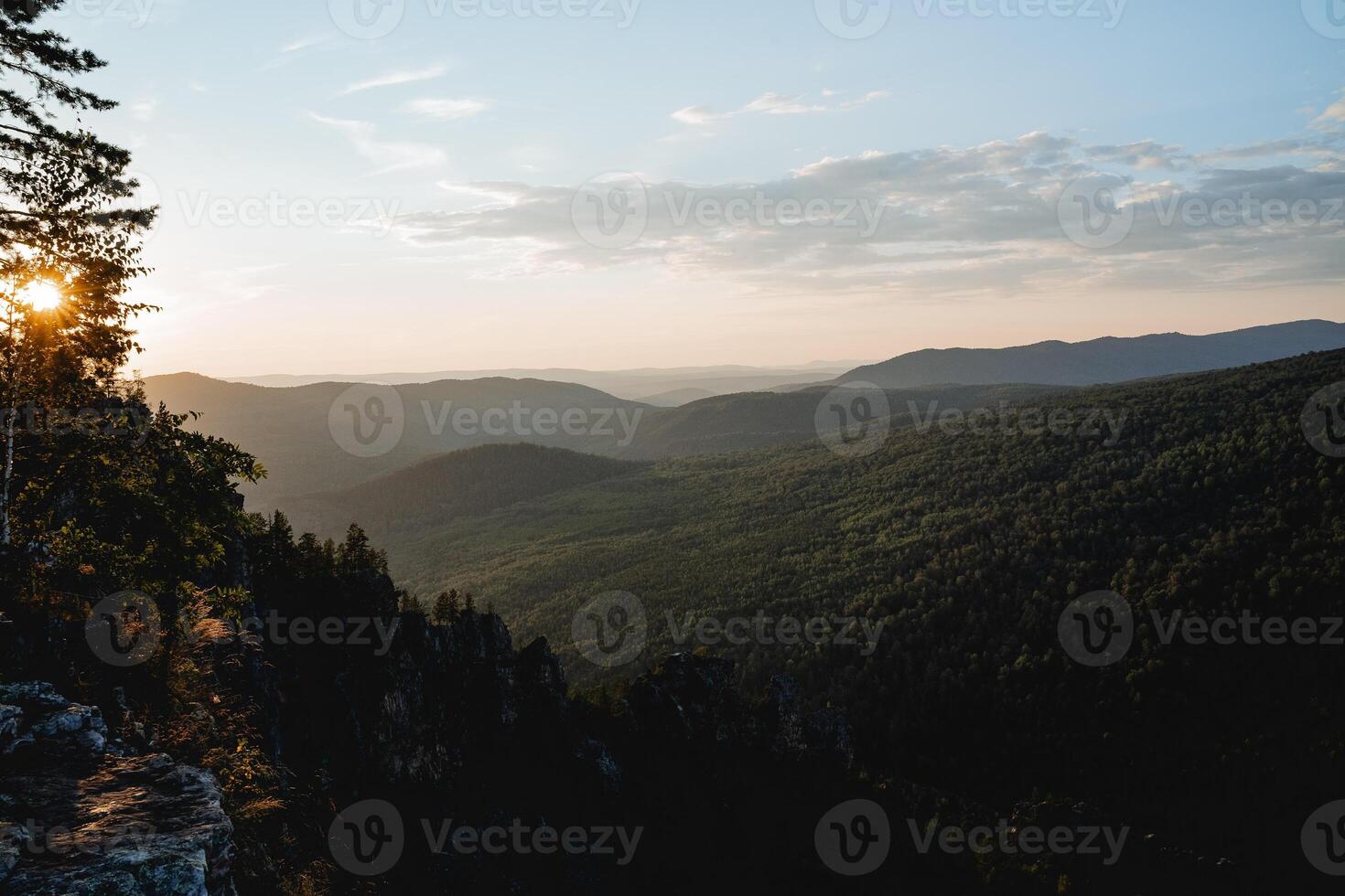 the landscape of the hilly mountains at sunset, the perspective of the horizon extending into the distance, the sun shining through the trees, the golden hour in photography. photo