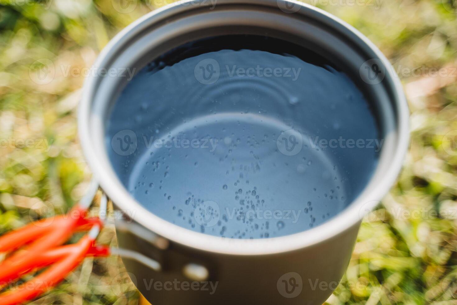 Tourist utensils for cooking in nature, a pot of water boils on the burner, air bubbles rise to the surface of the water, warm the tea. photo