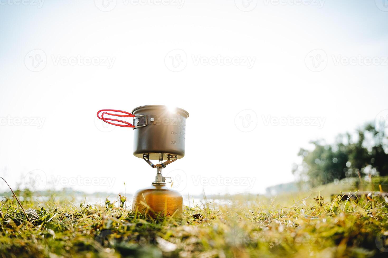 Tourist dishes stand on the grass against the background of sunset in the rays of sunlight, the pot stands on a gas burner, trekking in the forest, compact equipment for hiking, glare photo