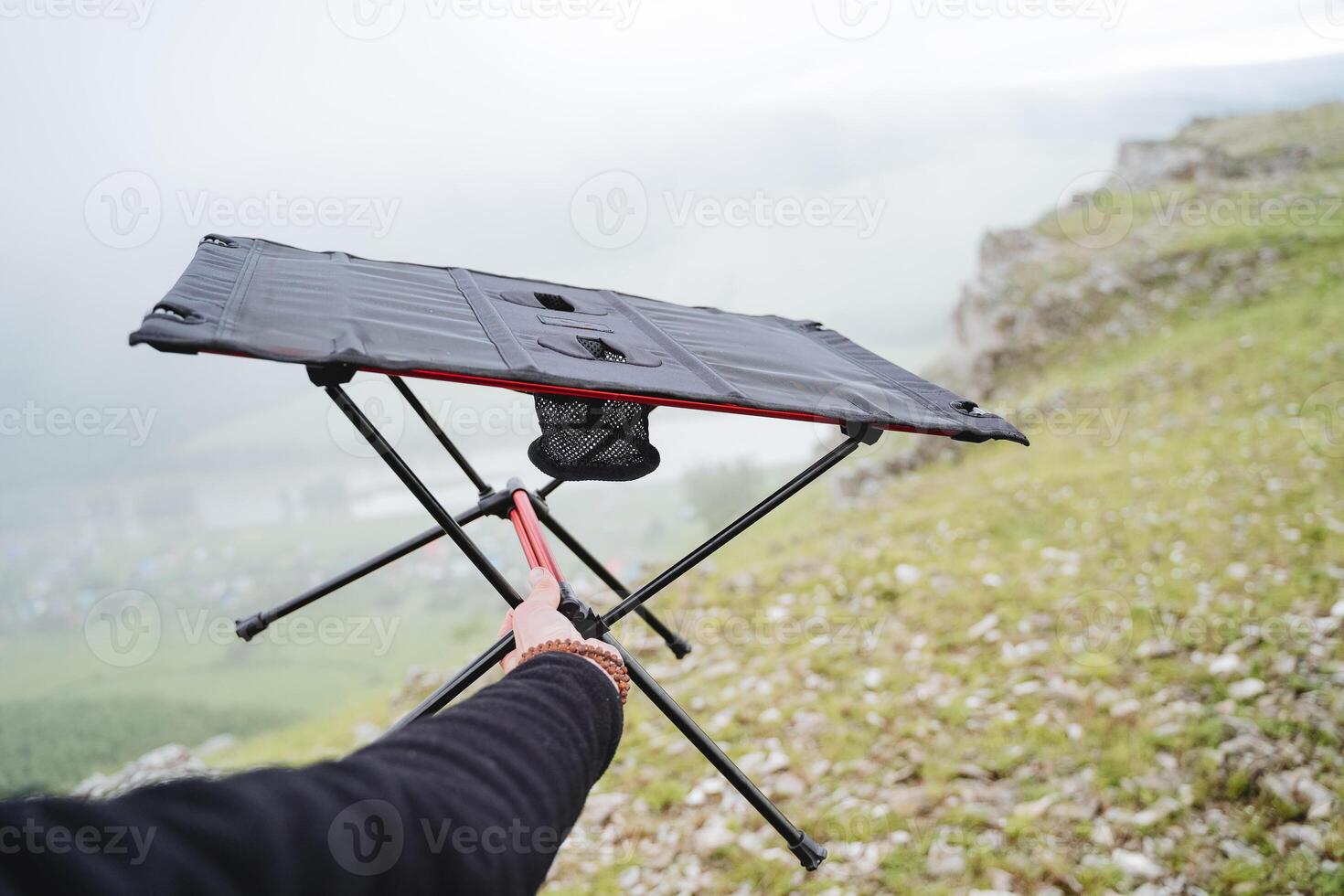 Compact folding table for camping in nature, camping equipment dining table, hand holds the frame of the table. photo