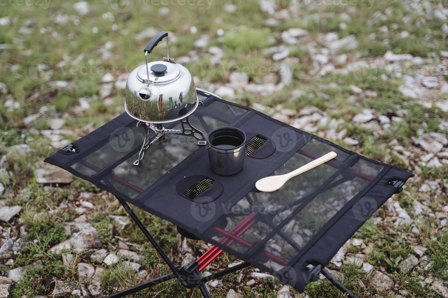 Camping furniture folding table made of netting, camping utensils, a glass of tea, a metal kettle stands on a gas burner. photo