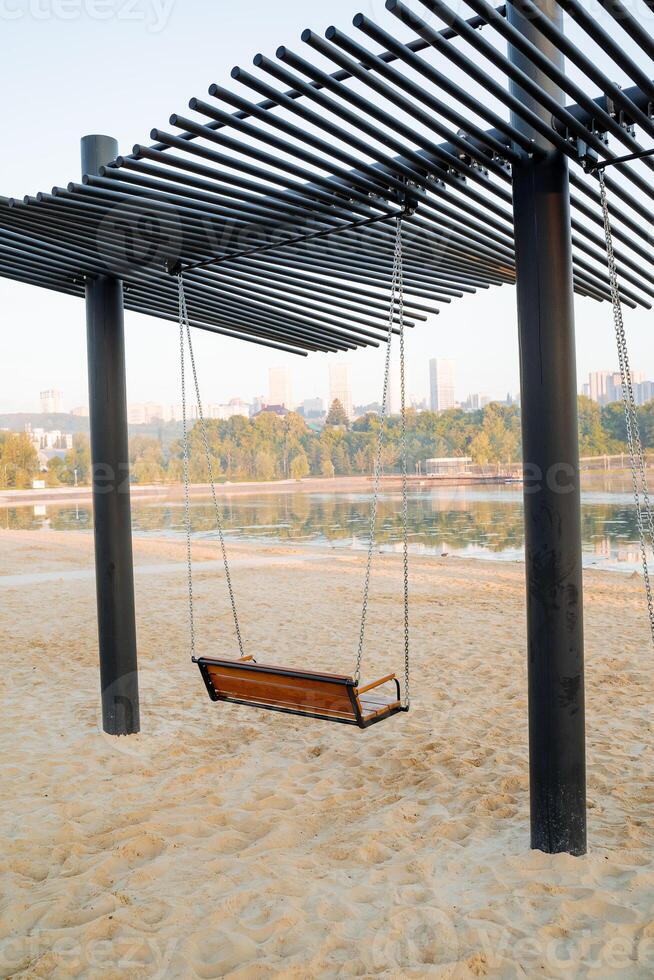 Beach swings, a suspended bench on chains for swinging, a large swing on the shore of the lake, a city amusement park, outdoor recreation. photo