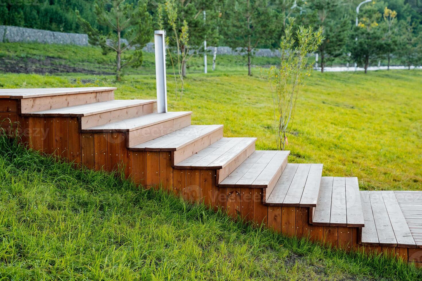 The concept of a wooden staircase in the park, steps from boards, a city park, a lawn near the house, morning light, a flat lawn, a wooden product. photo