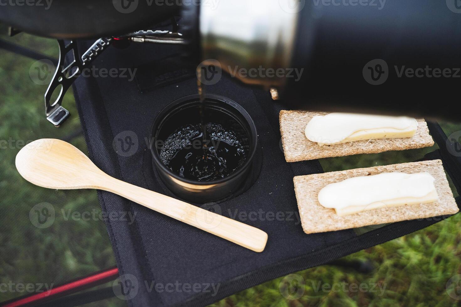 Pour hot tea from a thermos into a glass, a view of the pouring water on top of a mug, a wooden spoon on the table, butter sandwiches, food on a hike. photo