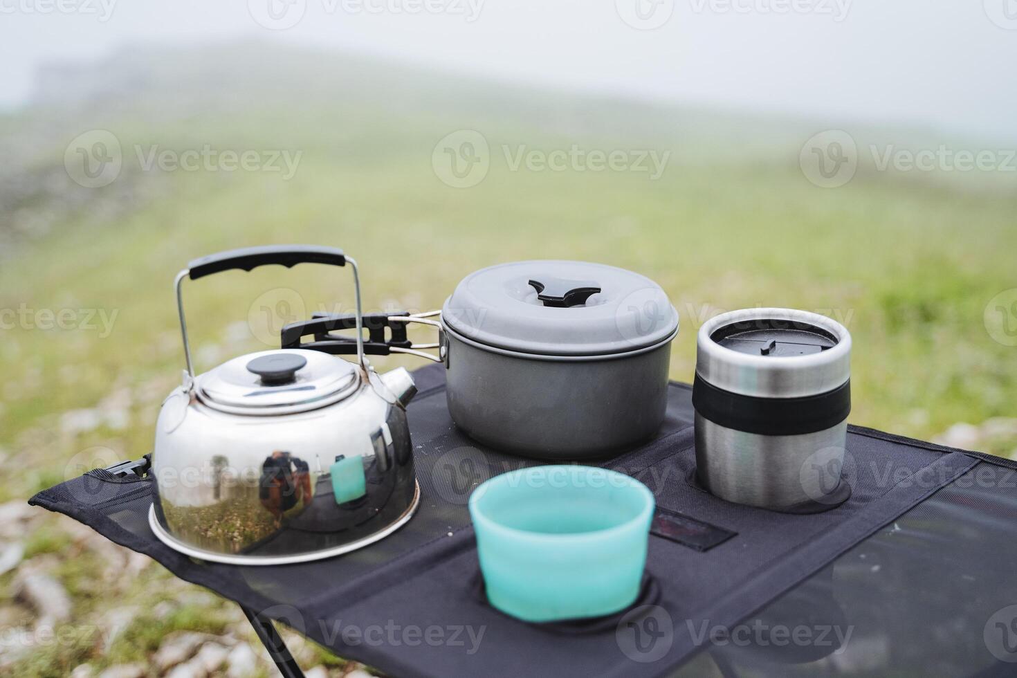 Camping utensils, a tourist metal kettle, a set of dishes, a glass of plastic, an iron pan. photo