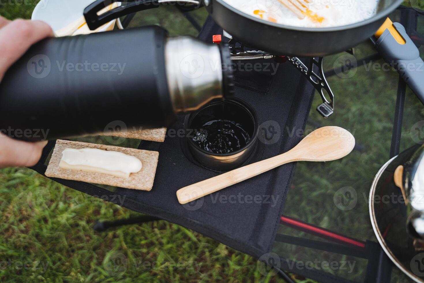 A hand holds a thermos pouring tea into a mug, a view from the top of the tourist utensils, outdoor recreation, food on the table at the campsite, a hot drink flowing in a cup. photo