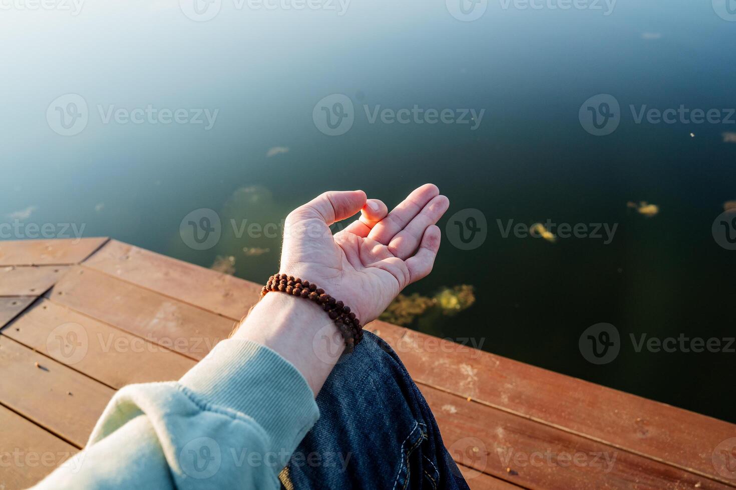 A man's hand is assembled into a chinmudra, a guy practices yoga meditation sitting on a pier, morning meditation, body part, rudraksha bracelet, yoga signs. photo