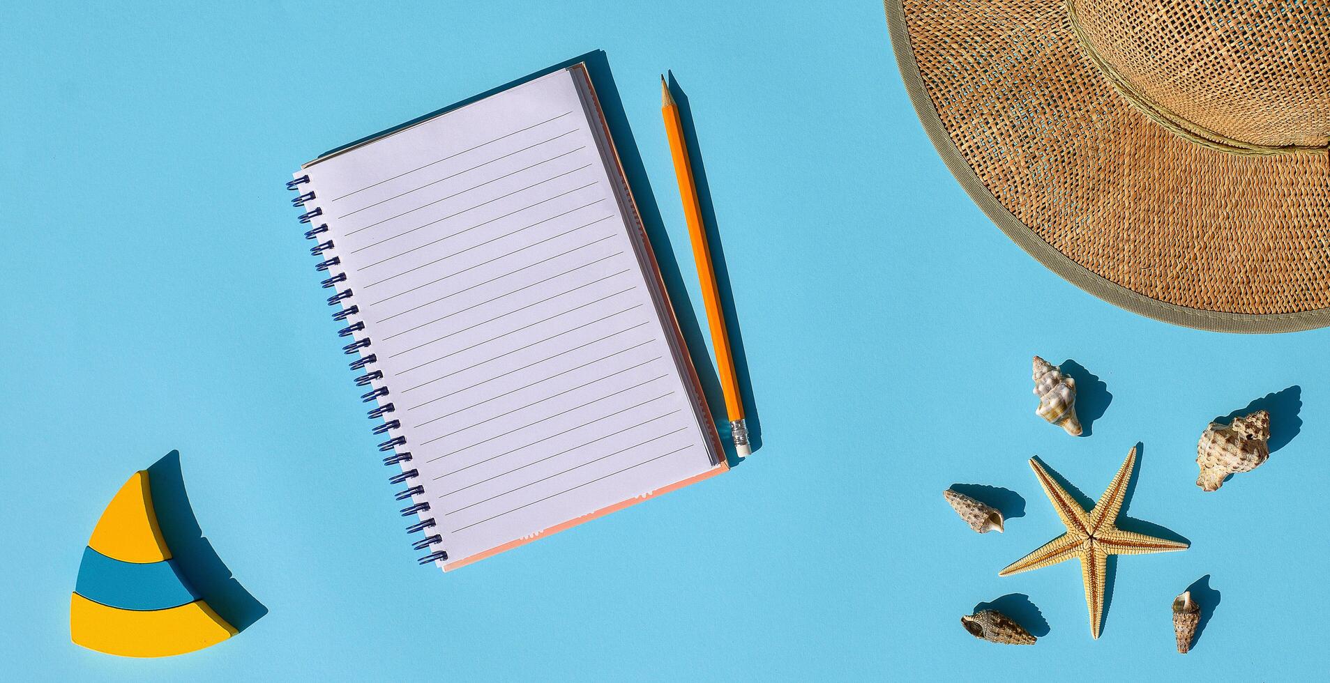 verano plano laico bandera con cuaderno con blanco. Paja sombrero, amarillo azul de madera barcos, mar conchas y estrella de mar en azul antecedentes. verano concepto, parte superior vista, Copiar espacio. centro de deportes acuáticos estilo composición. foto