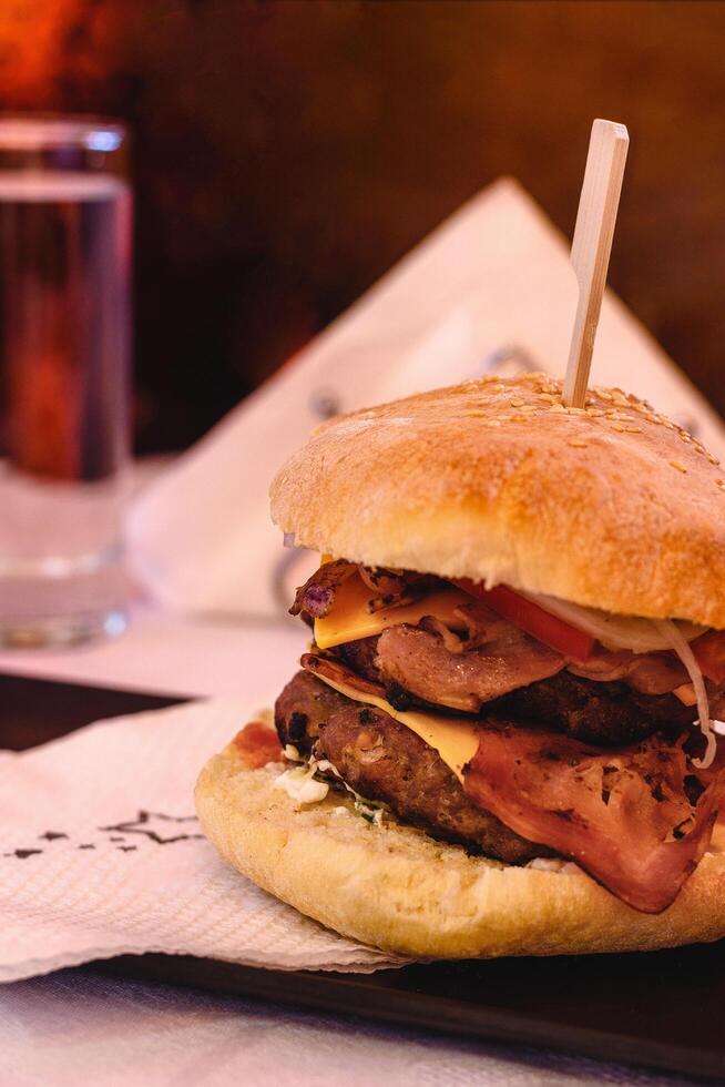 Vertical view of Double Burger with double beef or chicken burger, tomato, onion, lettuce, cheese, bacon and sauce served on black plate on white background in greek tavern. Selective soft focus photo
