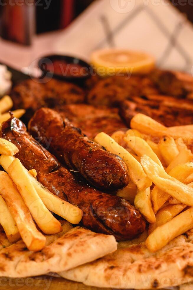 Vertical view of Close-up of Mix Grill Includes chicken leg, pancetta, sausage, bacon, burger, potatoes, sliced pita served with lemon and sauce in greek tavern. Selective focus. Mediterranean cuisine photo