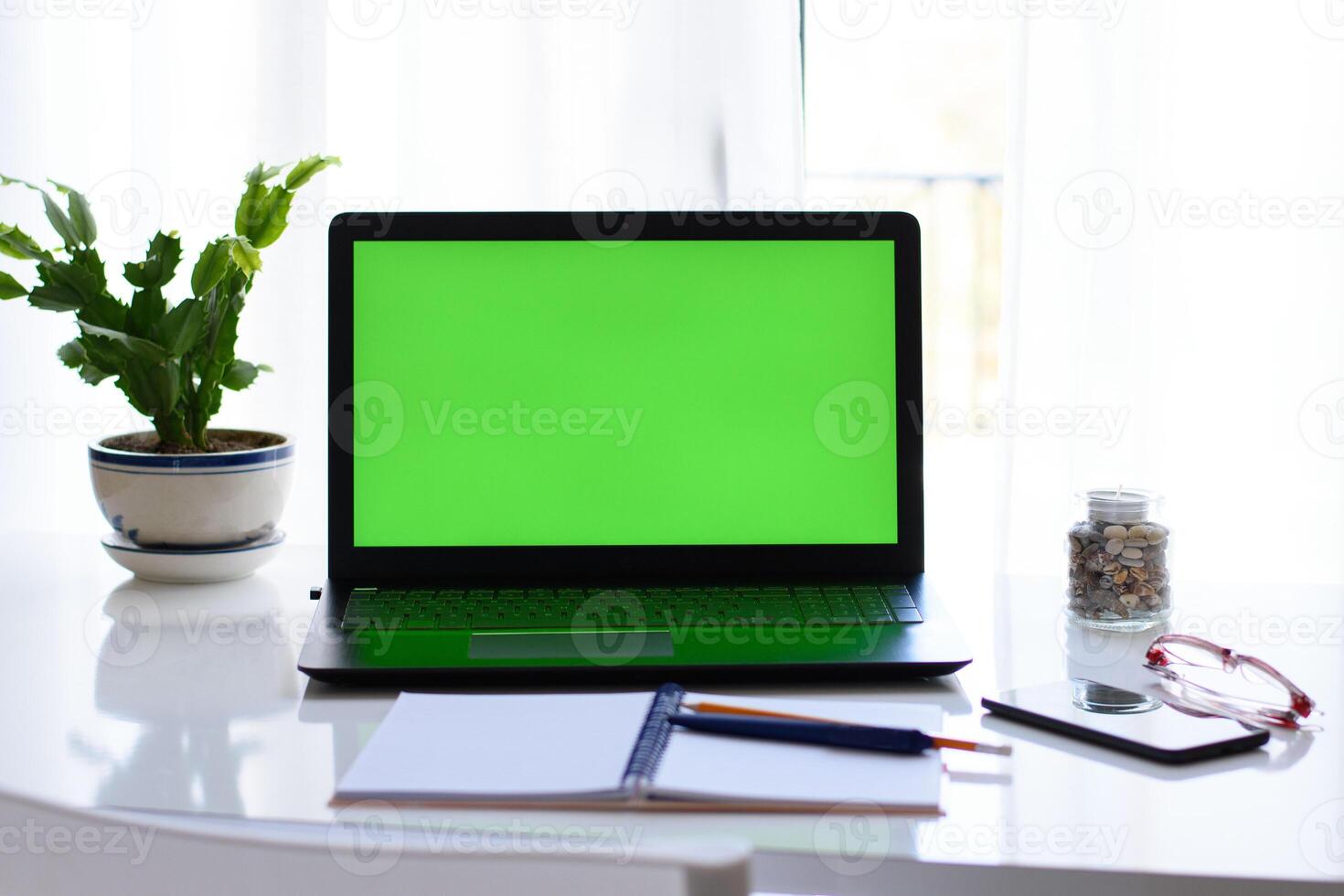 green screen on laptop. Concept of distance education, work environment. notebook, pen, smartphone, glasses, flower on the table in front of window. photo