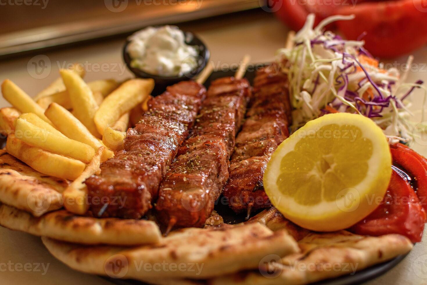 Plate with juicy mouthwatering pork souvlaki roasted on a BBQ grill, served with potato, pita, salad, tomato, lemon and sous in greek tavern. Selective soft focus. Mediterranean cuisine photo