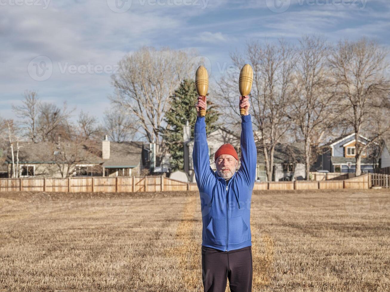 senior athletic male is exercising with wooden Indian clubs photo